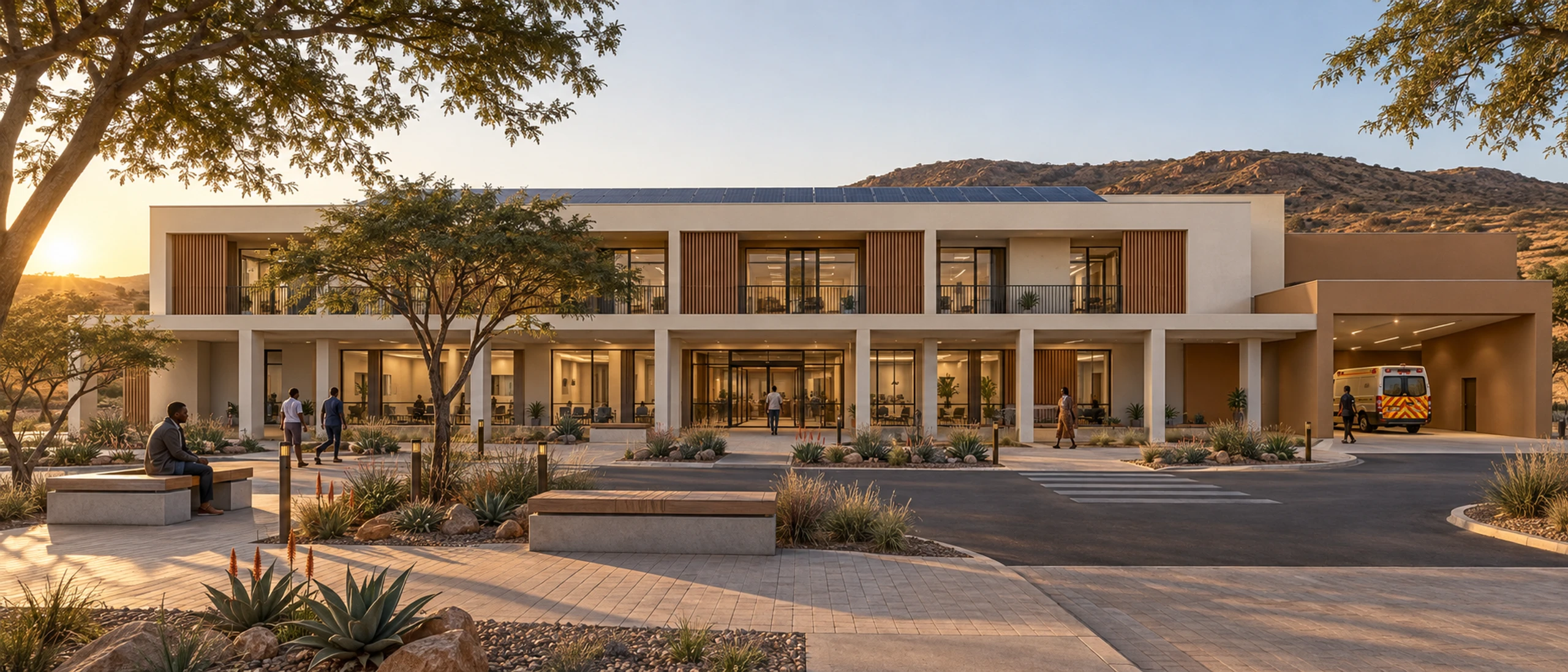 Two-storey precast clinic with a colonnaded ground floor and an ambulance bay at golden hour.